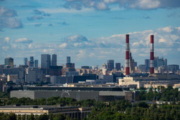 Fototapeta premium Epic industrial power plant chimneys Moscow city landscape panorama. Cinematic horizontal view of red and white factory smokestacks, urban financial district buildings, corporate skyscrapers and clo