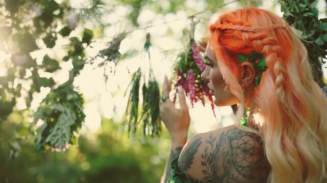 woman healer hand touches bunches of dry grass wind blow hair, dries herbs flowers plants for essential oil medicinal tea. Fairy girl beauty face. green forest summer nature trees magic sun rays light