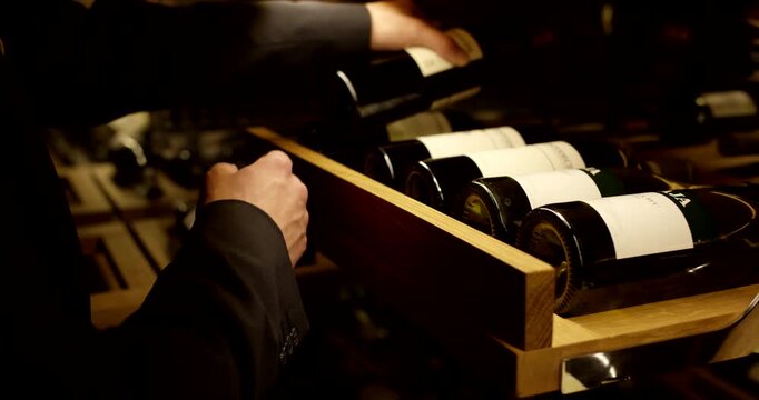 Close-up of a person selecting and pulling out a bottle of red wine from a modern wooden cellar rack