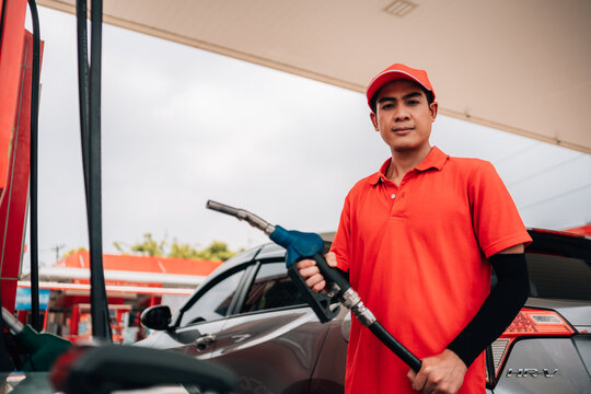 male gas station attendant looking directly at the camera with a confident, approachable expression. He is wearing a polo shirt and a matching cap,he is holding a fuel pump nozzle with a blue handle.