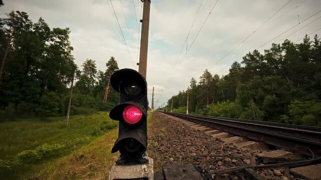 A red railway traffic light stands out against the railway track background, signaling a forced stop. This prohibitory signal serves as a metaphor for restrictions, guiding train operators to halt