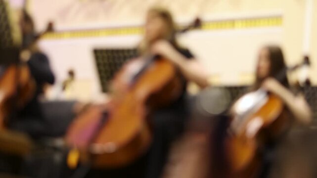 Blurred background shot of musicians playing cellos in a symphony orchestra