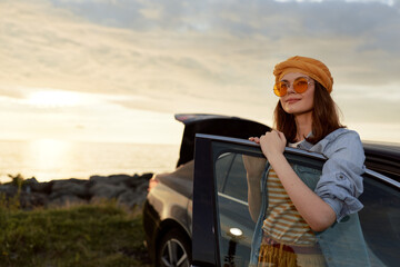 Naklejka premium Bright woman outdoors by a car at sunset, showcasing a relaxed lifestyle pose with hat and sunglasses, gentle breeze, warm golden light, natural colors and calm confidence