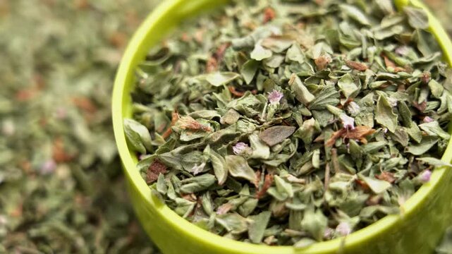 Dried oregano (Origanum vulgare) seasoning in a small plastic container. Organic herbal Ingredient in Mediterranean cuisine. Macro. Rotation