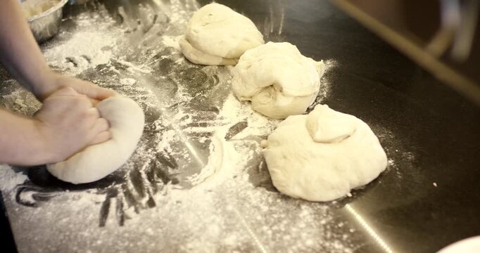 High angle view of a person shaping a dough ball on a floured countertop next to other pieces