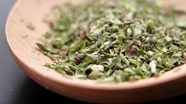 Dried crushed organic oregano leaves heaped on a rustic wooden spoon. Classic culinary seasoning. Mediterranean herb. Macro. Rotation