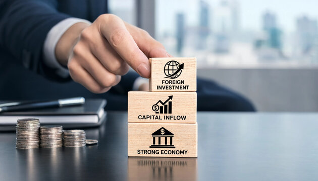 Businessman placing wooden block with foreign investment icon on top of capital inflow and strong economy blocks with coins and office supplies on table in office transparent background