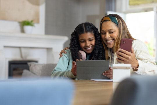 Female parent and adolescent leaning in at wooden table, viewing tablet while parent holding phone