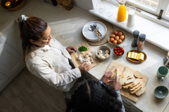 African American woman and teen girl chopping mushrooms, slicing bread on cutting board in kitchen