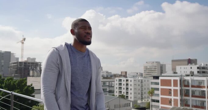 Mid-adult African American man leaning on railing, turning to camera and smiling, relaxing on roof