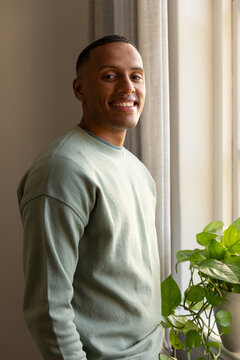 African American adult man standing near window facing camera at home with plant and hoop earring