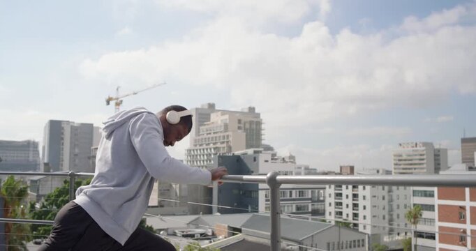 African American man leaning on railing on rooftop warming up for workout wearing headphones
