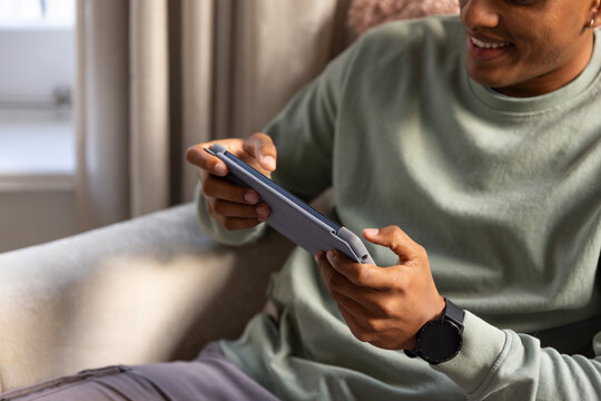African American man sitting on light-colored sofa by window holding tablet in folio case smiling