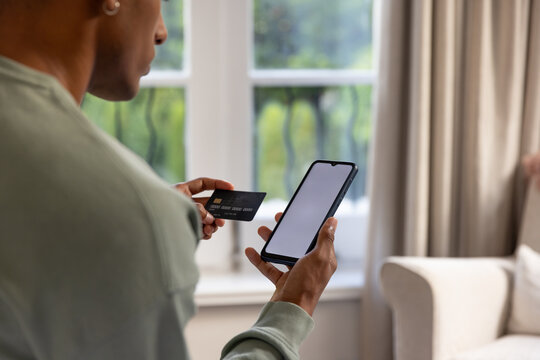 African American man holding phone and card near window at home, in green sweatshirt, hoop earring