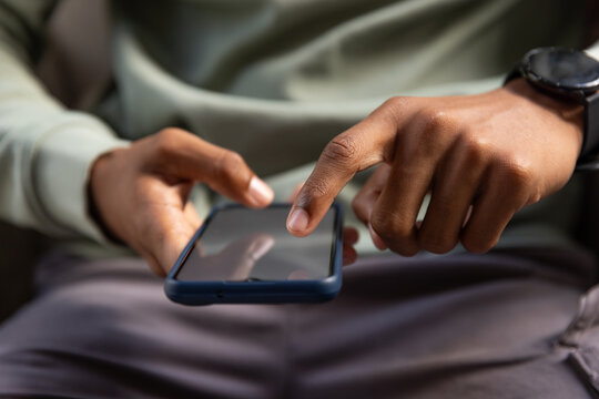 Man holding blue-case phone tapping screen, seated on couch wearing green top, black watch visible
