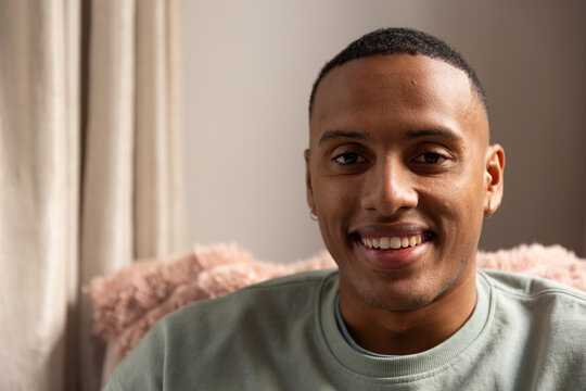 African American man in 20s smiling while sitting on couch with blush pillow showing hoop earrings