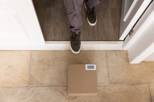 African man wearing grey cargo pants, sneakers, standing at doorway near barcode box on stone porch