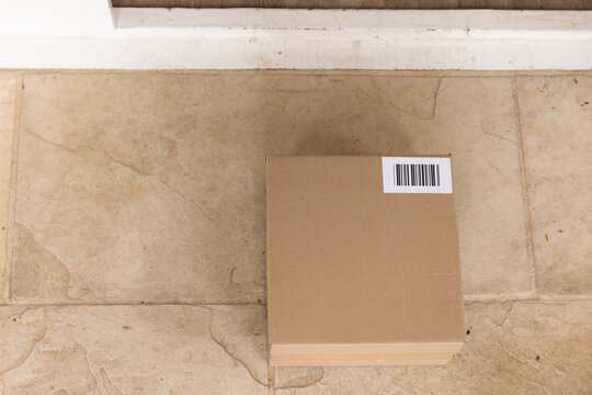 Sealed corrugated cardboard box is sitting on beige stone doorstep near white door trim