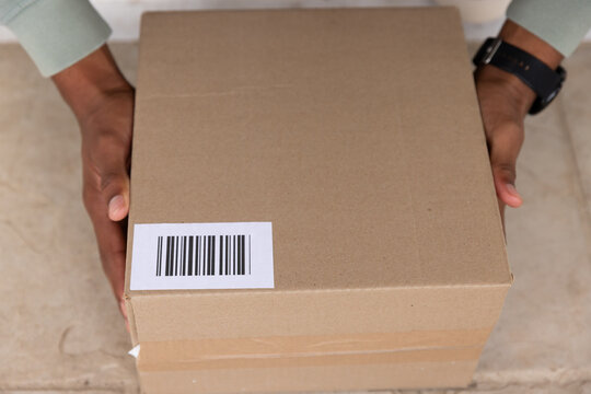 African American man holding cardboard parcel on tiled porch, presenting barcode label and watch