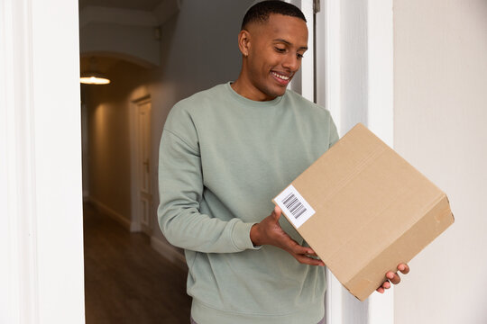 African American man holding cardboard box with barcode at door, warm hallway light, hardwood floor