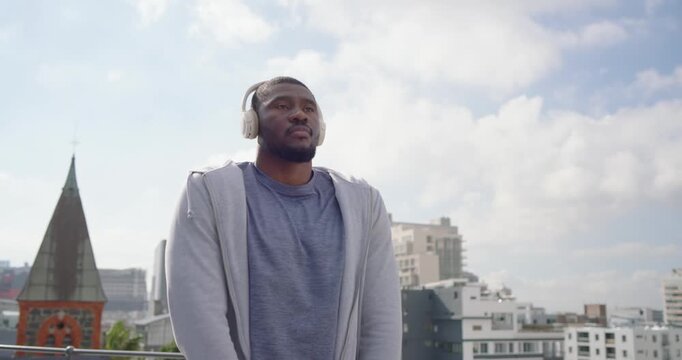 African American man breathing deeply adjusting hoodie headset stretching on roof rail before run
