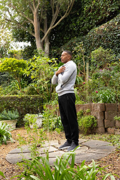 African American adult man standing on stone ring in garden in gray sweater, gray sneakers