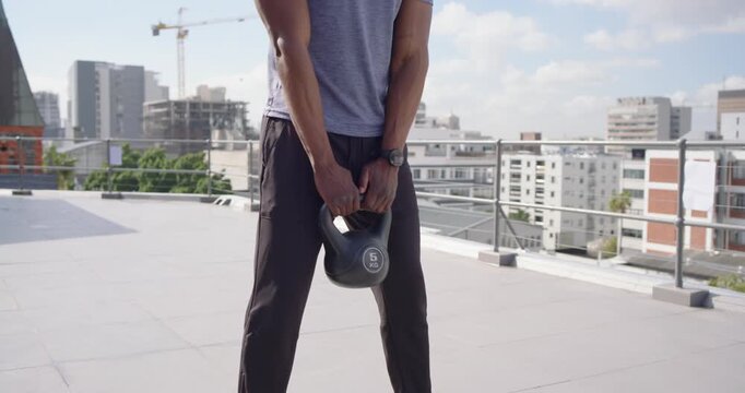 African American man shifting weight, swinging kettlebell on rooftop to build strength