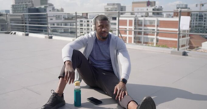 Mid adult African man reaching for teal water bottle, checking smartwatch, cooling down on rooftop