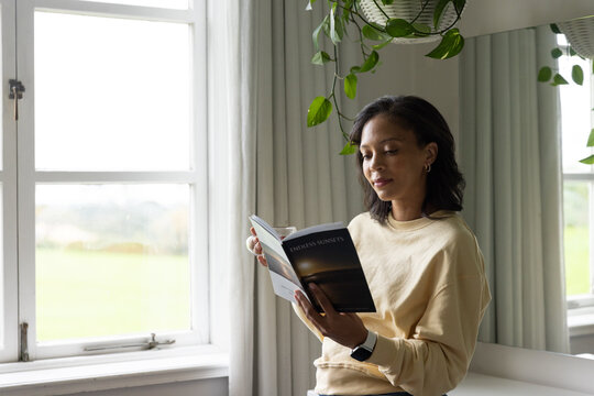 African woman reading ENDLESS SUNSETS in room near window with hanging plant sweatshirt, copy space
