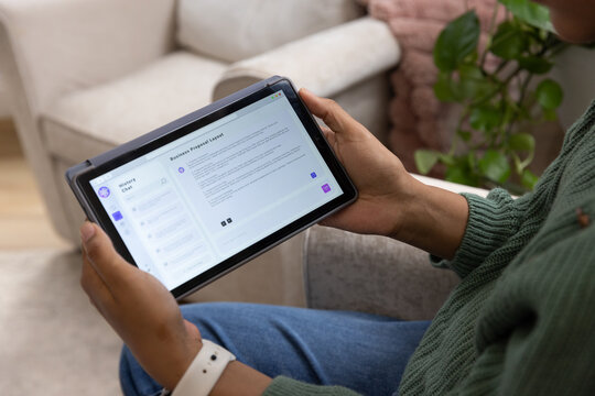 Female holding tablet and reviewing document on sofa at home wearing green sweater, smartwatch