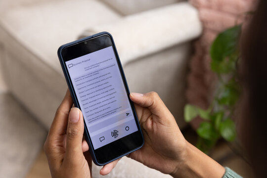 African American woman holding phone in navy case wearing green reading Business Proposal on sofa