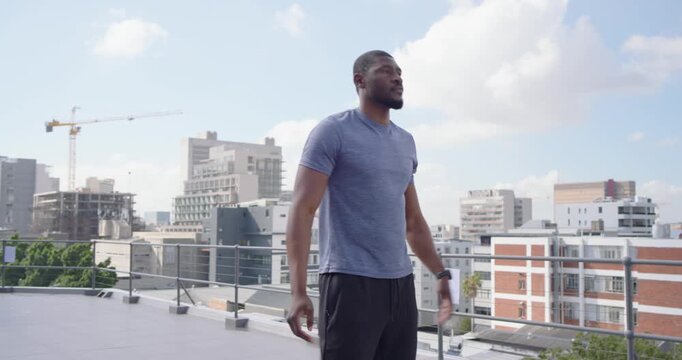 Mid-adult African man warming up in blue shirt then lifting kettlebell for fitness on roof