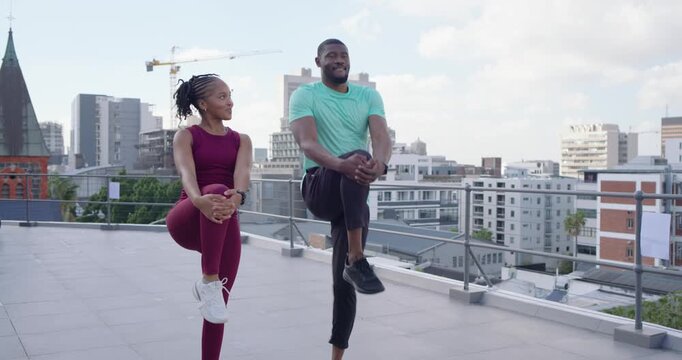 Workout pair facing lens doing knee and quad stretches, warming up on rooftop wearing wrist tracker