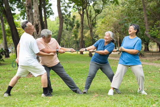Four cheerful seniors in a friendly tug of war on a vibrant green lawn showcasing their vitality, camaraderie, and Active Seniors lifestyle, enjoying an active and playful moment in a park setting.