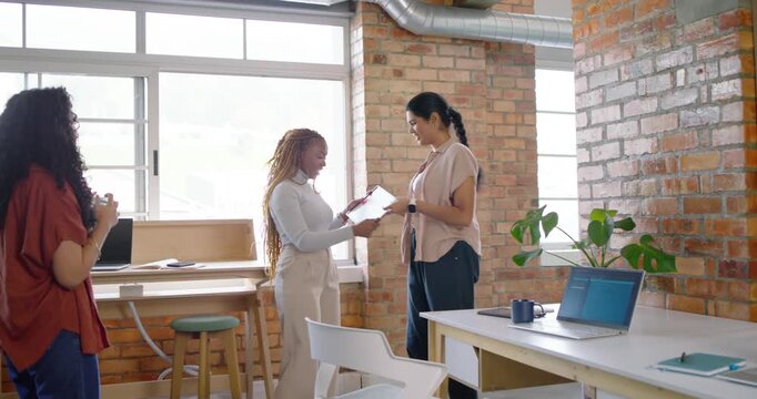Female duo exchanging framed plaque marking milestone, shaking hands in office as peer snapping pic