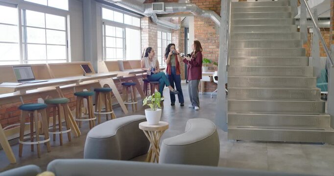 Diverse coworkers gathering around peer showing phone, holding cups on break in lounge, office wear