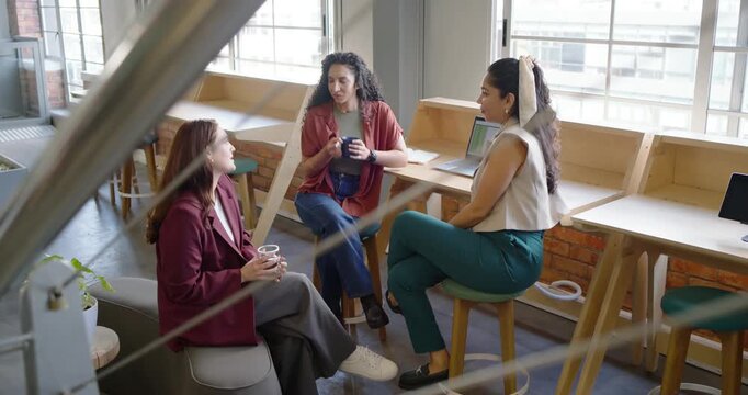 Diverse coworkers having coffee break, discussing project while gesturing, sipping mugs near laptop