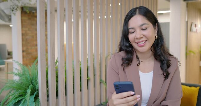 Adult woman sitting in office, reading phone and reacting to message with lapel mic on blazer