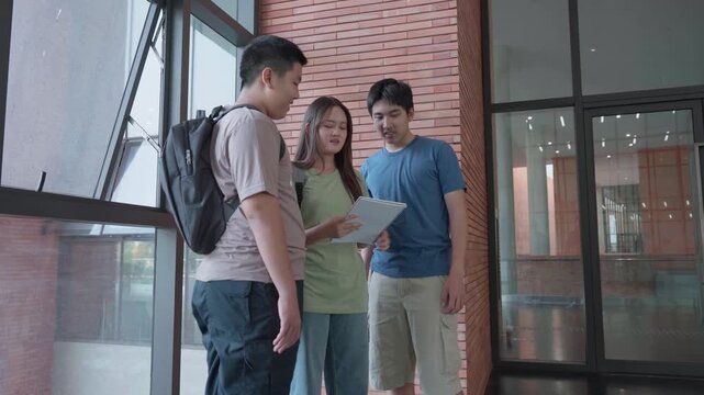 Academic Collaboration: Three students, immersed in collaborative study, stand near the architectural beauty of a modern building, their focus intently drawn to a digital tablet.