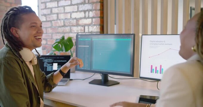 African American coworkers trading jokes while man pointing at left monitor code, reviewing chart