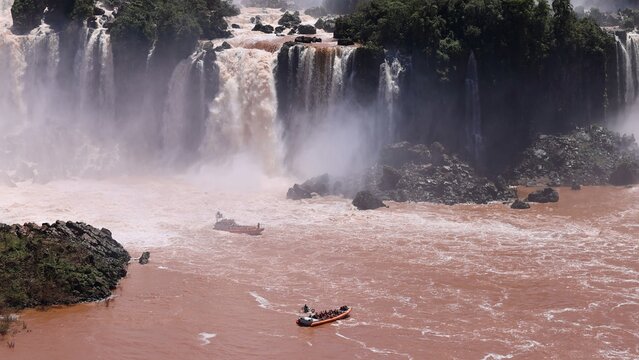 Aerial view of Iguazu Falls with powerful cascading water and tourist boats navigating the river in Foz do Iguacu, State of Parana, Brazil.