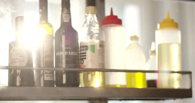 Assorted bottles of oils and condiments arranged on a shelf in a commercial kitchen