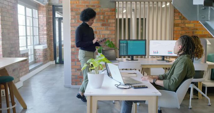 Presenter in black top walking, scanning tablet before presenting charts on monitors at open office