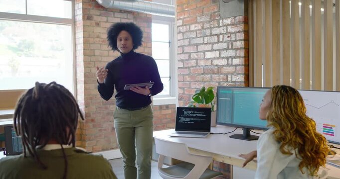 African American man tapping tablet leading meeting in office reviewing laptop code monitor charts