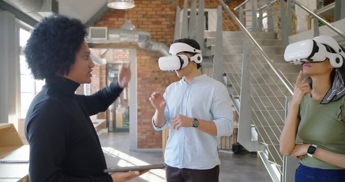 Diverse team trainer holding tablet starting VR demo in loft guiding two in white headsets training