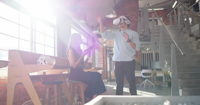 Diverse coworkers man putting on VR headset gesturing while woman guiding demo on tablet by windows