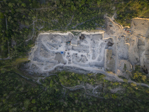 Aerial view of a sand and stone quarry surrounded by lush green forest, showing excavation paths and rocky terrain in Manisrenggo, Central Java, Indonesia.