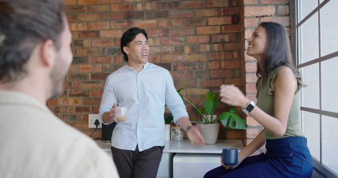 Diverse coworkers on break in kitchen, man starting chat holding clear mug, woman with blue mug