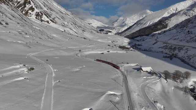 A Red Passenger Train is Running through Snowy Mountain in the Swiss Alps. Aerial View at sunny Day.