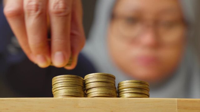 muslim woman stacking Gold Coins into Tower on Wooden Table Close Up, concept of investing